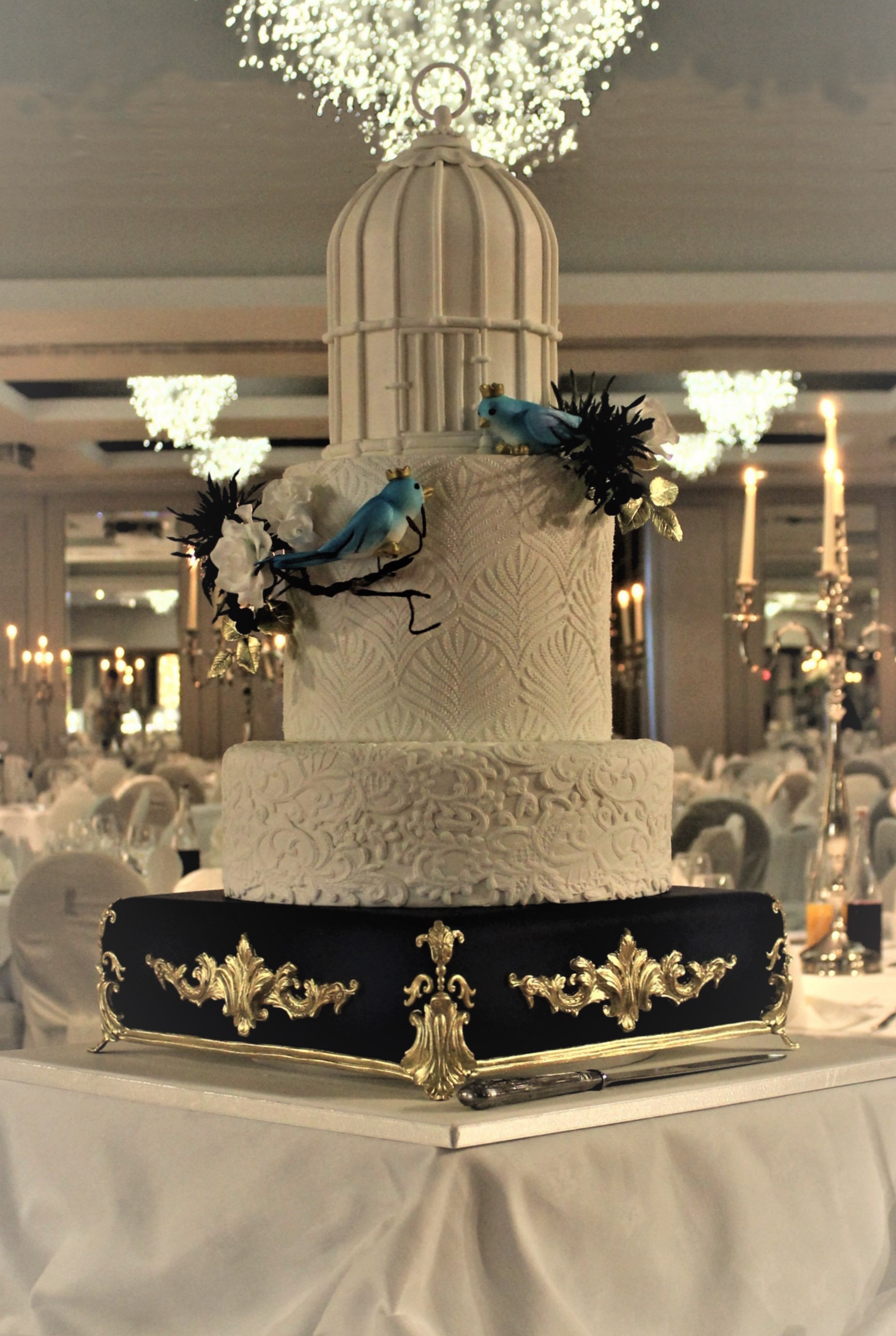 Love birds gazing into each other’s eyes on a tall, elegant, four-tier, wedding cake
