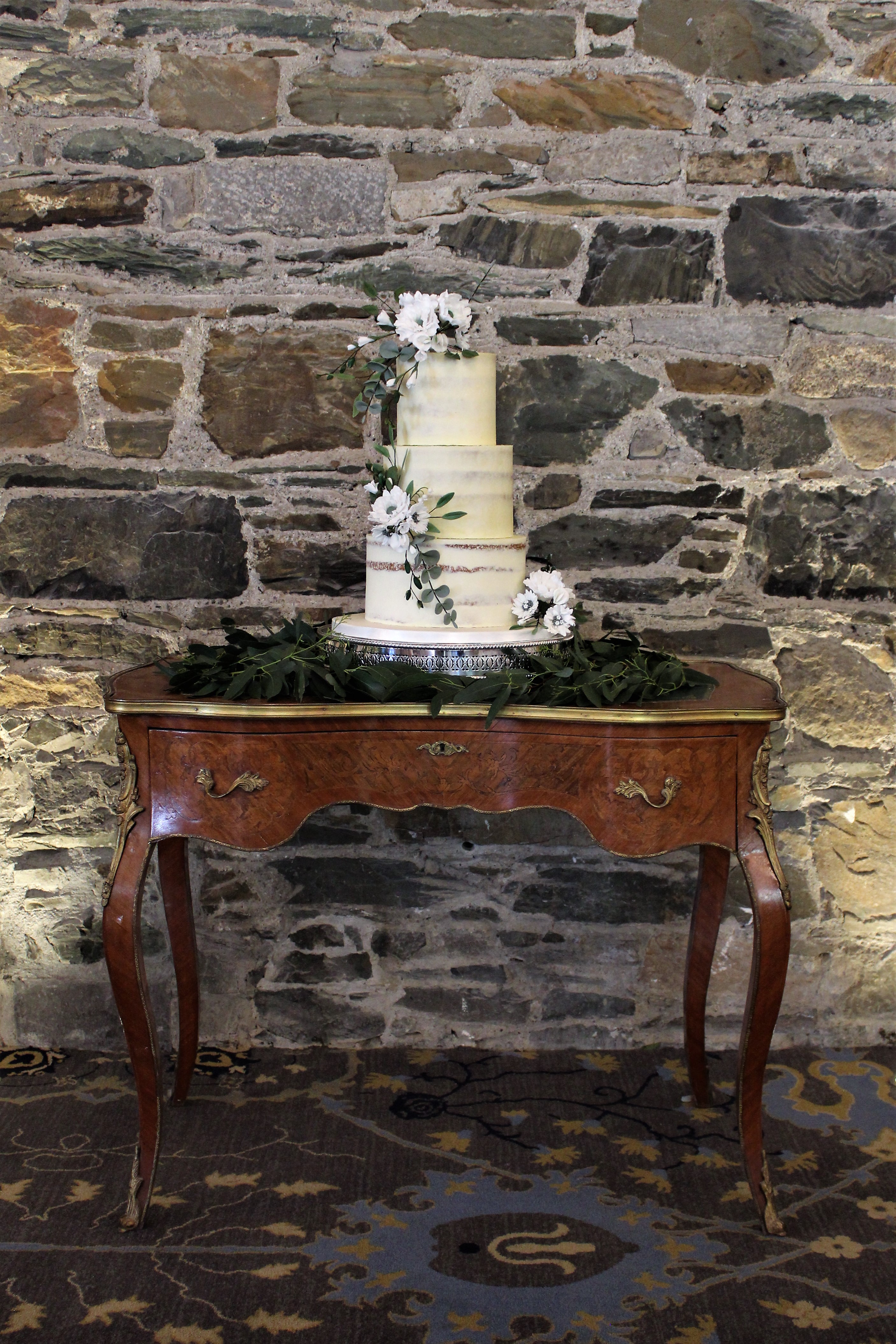 A semi-nude white three tiered cake finished with handmade sugar-flowers
