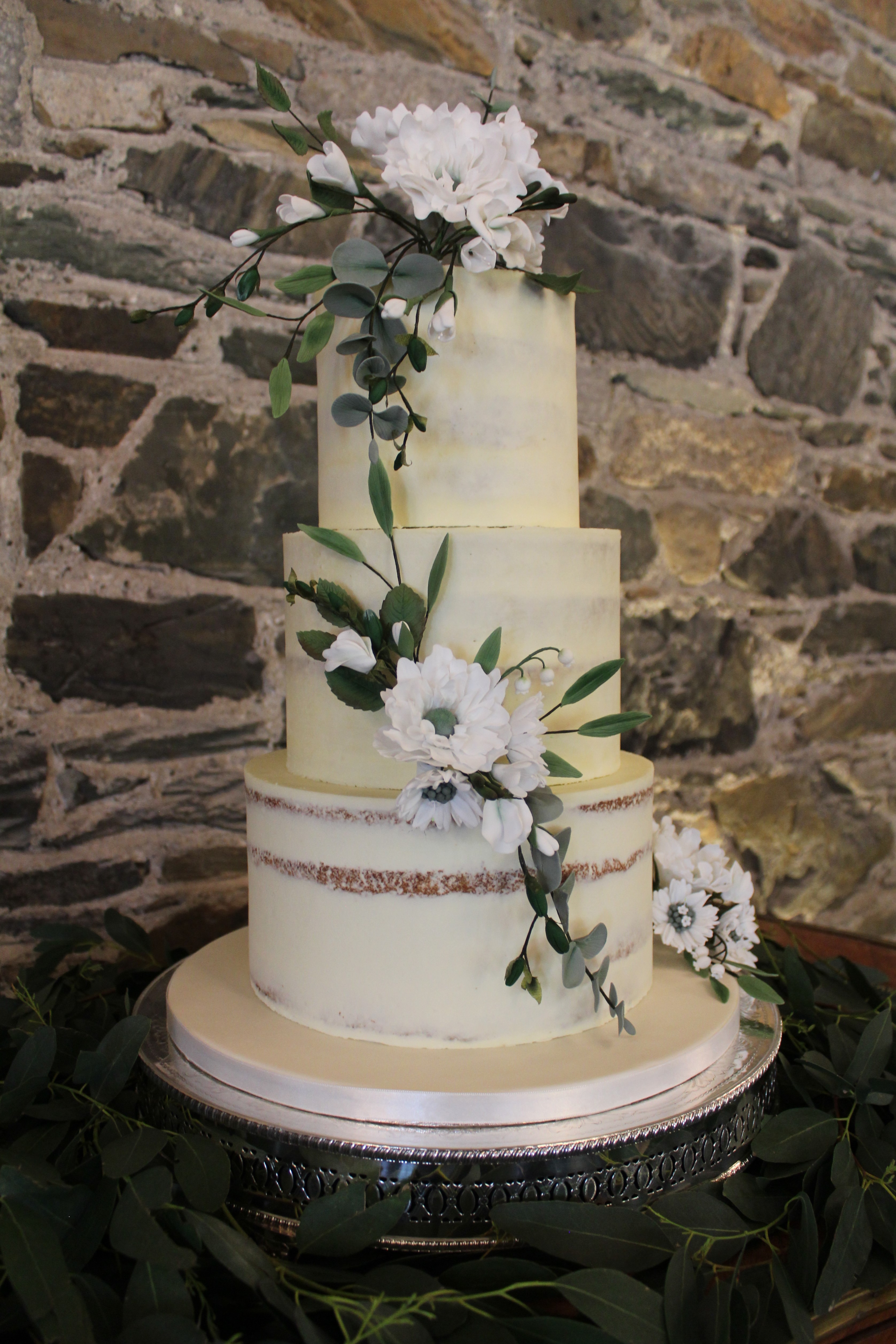 A semi-nude white three tiered cake finished with handmade sugar-flowers