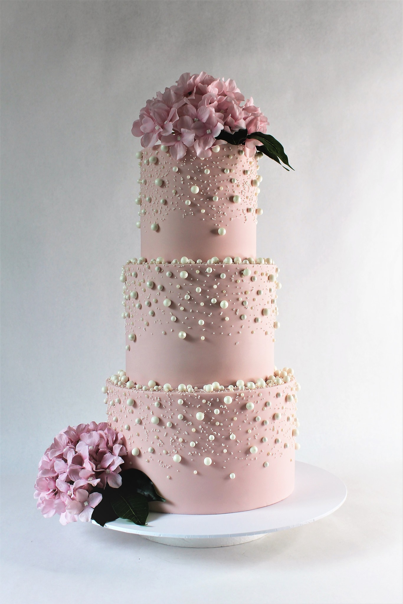 Three tiered pink cake with pearls adorned on the outside